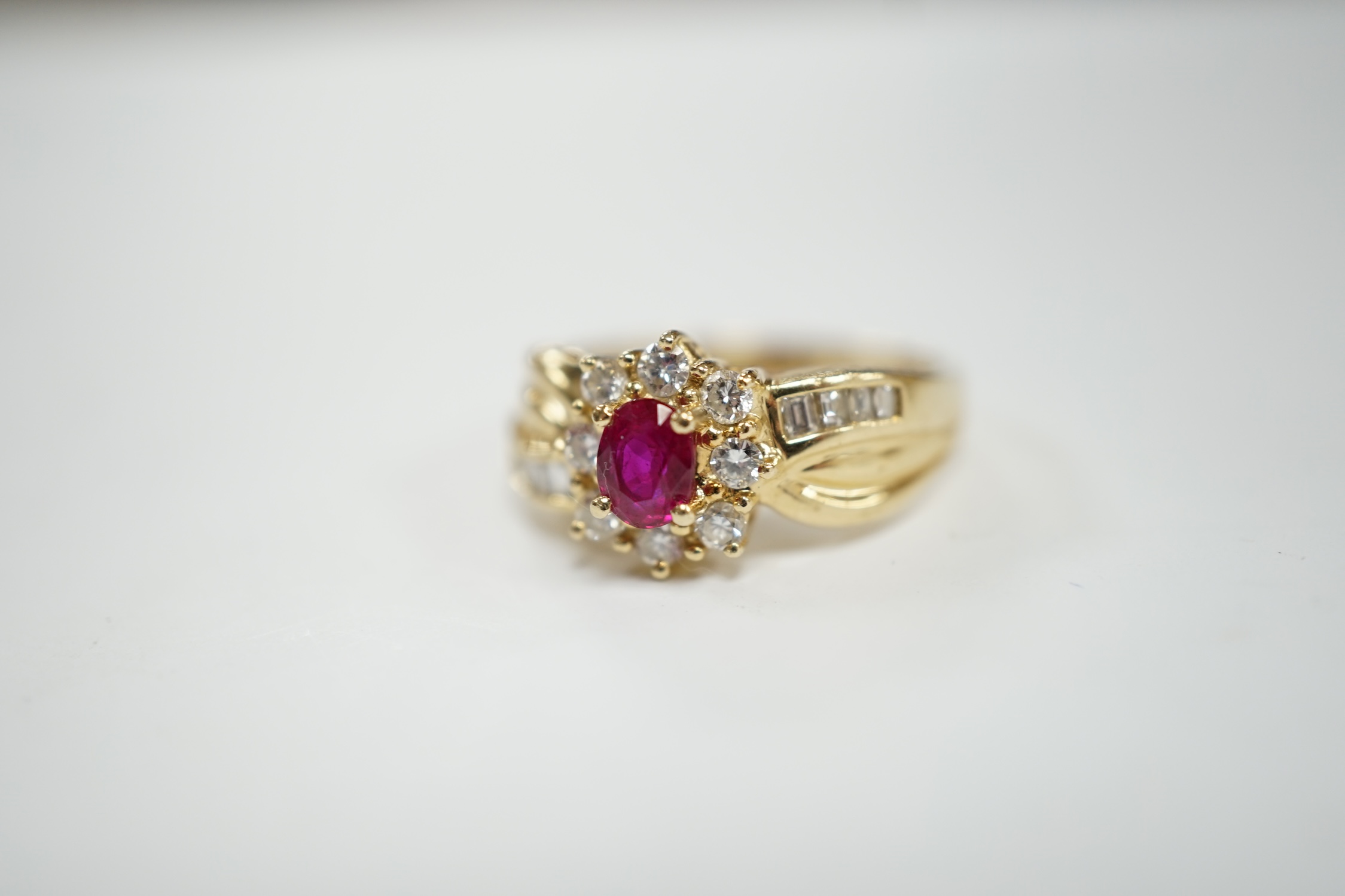 A modern 14k, ruby and diamond set oval cluster dress ring, with diamond chip set shoulders, size P, gross weight 5.1 grams.